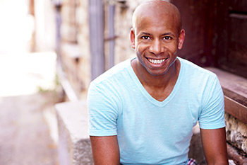 "Man shown from torso up. He smiles widely and looks at the camera. Limestone wall background"