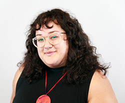"portrait of a woman with long curly hair and plastic rimmed glasses. She smiles and looks at the camera"